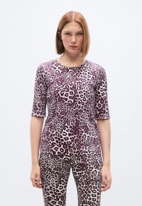 Μωβ και λευκό τοπ με λεοπάρ σχέδιο, μανίκια τριών τετάρτων και στρογγυλή λαιμόκοψη, συνδυασμένο με κολάν στο ίδιο μοτίβο. Ομαλή υφή υφάσματος.