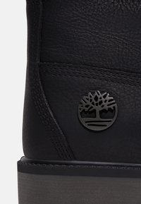 Must väljakujundusega mustad nahast saapad, mille peal on tikitud detailid ja ümmargune, embosseeritud must logo, millel on puu kujundus ülemises osas. Tugev, tekstuuriga tald.