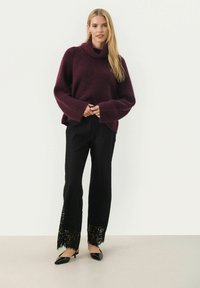 Bordeaux oversized gebreide trui met een rolkraag, gecombineerd met zwarte textuurbroek met kantaccenten aan de zoom en zwarte puntige ballerina's.