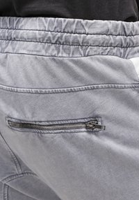 Šedé kalhoty s texturovanou tkaninou, s kapsou na zip na pravé zadní straně a elastickým pasem.