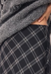 Pull gris tricoté porté sur une jupe à carreaux noire. La jupe présente des lignes à carreaux gris clair dans un motif structuré. Texture du tissu lisse visible.