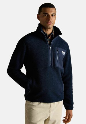 Marineblaue Fleece-Pullover mit hohem Kragen, halbem Reißverschluss vorne und einer Reißverschlusstasche auf der Brust. Texturiertes Material mit weicher Optik.
