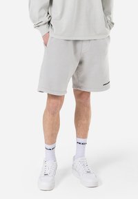 Shorts de color gris claro, confeccionados con tela suave, con un corte relajado y bolsillos laterales. Logo bordado "PEGA" en el dobladillo inferior.