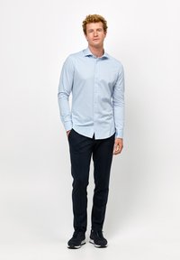 Lichtblauw langslavend overhemd met een slim fit en klassieke kraag, gecombineerd met donkerblauwe broek en zwarte sportieve schoenen.
