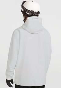 Witte buitenjack met capuchon, met een ruime pasvorm en elastische manchetten, ontworpen voor winteractiviteiten. Zwart merkembleem op de kraag.