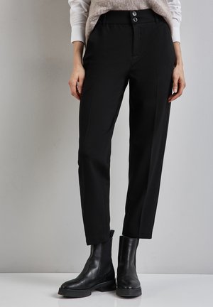 Pantaloni neri su misura con vita alta, dotati di due bottoni, gamba dritta e tasche laterali. Indossati con stivaletti neri in pelle appena sopra la caviglia.