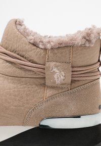 Bota de cuero marrón con un cuello suave y peludo, detalle de logo en relieve y suela en blanco y negro contrastante con un acento brillante.