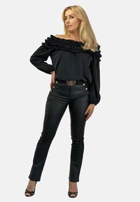 Czarny top na ramiączkach z falbaniastym dekoltem, w zestawieniu z dopasowanymi czarnymi skórzanymi spodniami i sandałami na szpilce, podkreślony pasem z złotymi akcentami.