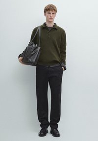 Ciemnozielony sweter dziany z kołnierzem, czarne spodnie i czarne buty. Modelka trzyma torebkę z fakturowanej czarnej skóry.