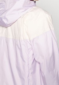 Lichtpaarse hooded jas met een kleurgeblokkeerd ontwerp, met een gladde textuur en een elastische tailleband. De achterkant laat een relaxte pasvorm zien.