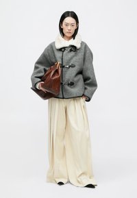 Sivi vuneni kaput s duplim zatvorenim čepovima i bijelim krznom oko vrata, uparen s bijelim plisiranim hlačama i smešnom kožnom torbom.