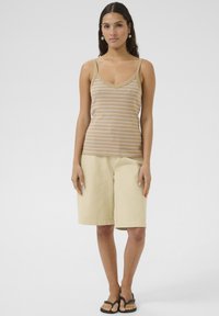 Puuvillane tank-top pruunide ja valgete triipudega, kombineerituna beežide põlvekõrguste lühikeste pükstega, seljas mustad flip-flop sandaalid modellil.