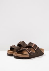 Sandales en daim marron avec deux brides réglables et boucles en ton cuivre. Semelle en liège profilée et semelle extérieure en caoutchouc texturé.