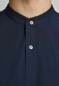 Maglietta blu navy con colletto, caratterizzata da una patta con bottone con due bottoni argentati, realizzata in un tessuto liscio con una finitura leggermente testurizzata.