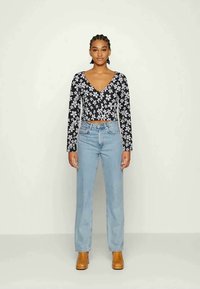 Top cropped de manga longa floral preto com decote em V, combinado com jeans de perna reta azul claro e botas de tornozelo castanhas, sobre um fundo neutro.