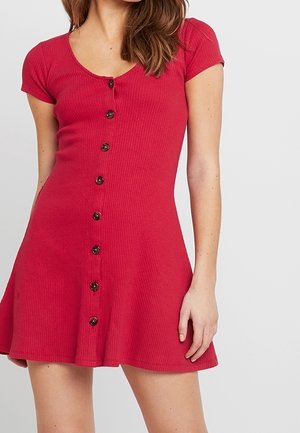 Vestido corto de manga corta en rojo con costillas, con escote redondeado y cierre de botones en la parte delantera. Silueta de falda acampanada, textura suave y botones redondos.