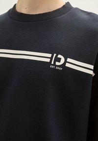 Felpa navy con collo a girocollo ribattuto, presenta due strisce orizzontali bianche e un logo con "EST. 2007" al centro. Tessuto morbido.