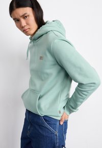 Mint green hoodie with a front pocket, adjustable drawstring at the hood, and small logo on the chest. Soft fabric with a relaxed fit.