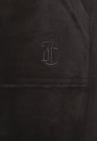 Tissu en daim noir avec un logo brodé. La texture est douce avec une finition mate, mettant en valeur des coutures délicates et un détail de poche.