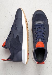 Pair of navy blue sneakers with orange accents, textured soles, and dark blue laces, displayed on a light concrete surface.