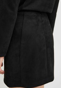Schwarzes Kunstsuede-Kleid mit glatter Textur, einer Seitennaht-Detail und einem leicht ausgestellten Saum. Hat einen lockeren Schnitt.