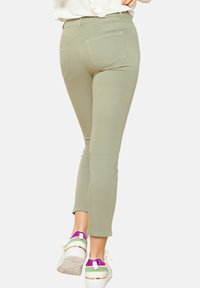 Khaki skinny hlače z gladko teksturo, ki imajo zadnje žepe in so v kombinaciji z belimi supergami z vijoličnimi in zelenimi detajli.