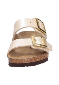 Sandalia deslizante de cuero beige que presenta dos correas anchas con hebillas doradas, plantilla de corcho y suela exterior de goma texturizada marrón.