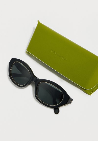 Lunettes de soleil noires oversize avec verres foncés, posées à côté d'un étui rigide rectangulaire vert avec un embossage subtil de la marque, sur un fond blanc.