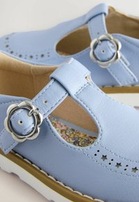 Scarpe in pelle azzurro chiaro con fori e una fibbia argentata a forma di fiore. Soletta con motivo floreale e suola bianca con bordo marrone.