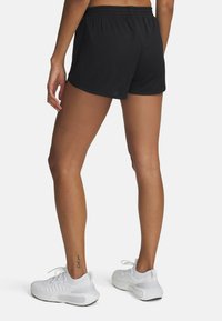 Pantalones cortos atléticos negros con un diseño de malla texturizada, una cinturilla elástica y un ajuste relajado, acompañados de zapatillas blancas.