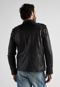 Zwarte leren jas met een slim fit ontwerp, ritssluitingen en schouderaccenten. Soepele textuur met gestikte details. Casual stijl.