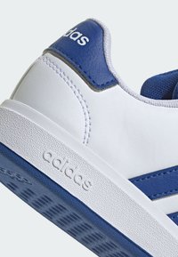 Basket blanche avec des accents bleus, fabriquée en matériau synthétique ; présente une semelle texturée, des détails cousus et une marque en relief.