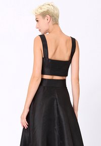 Top court en satin noir avec de larges bretelles et un dos carré, associé à une jupe taille haute assortie. Texture lisse et design minimaliste.