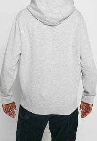 Sudadera gris con capucha, que presenta una textura suave y mangas largas. El dobladillo y los puños son acanalados para un ajuste ceñido. Sin logotipos ni patrones visibles.