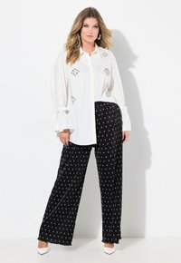 Witte button-up shirt met decoratieve rhinestones en brede mouwen; gecombineerd met zwarte broek met stippen en witte puntige hakken.