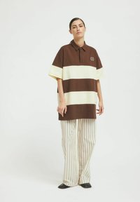 Brun och gräddfärgad randig oversized polo med krage, som har en liten logotyp. Kombinationen med vida randiga byxor i beige.