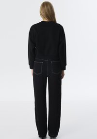 Sudadera corta negra con escote redondo combinada con pantalones negros de talle alto y plisados que cuentan con costuras blancas y bolsillos traseros.