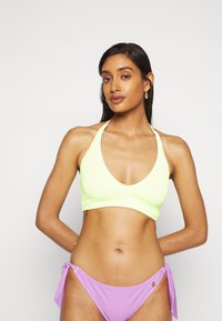 Top de bikini em amarelo néon, com textura canelada, um decote em V profundo e alças halter, emparelhado com calções de bikini lilás com laterais ajustáveis e um detalhe decorativo.
