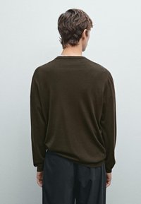 Brauner, langärmliger Pullover aus weichem Material, mit lockerer Passform und einfachem Rundhalsausschnitt. Kombiniert mit schwarzen Hosen.