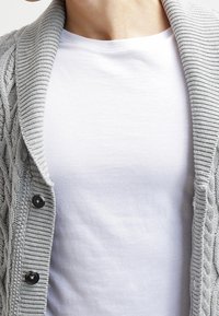 Gray knitted cardigan with a textured cable pattern, featuring a wide shawl collar and black button accents, worn over a plain white shirt.