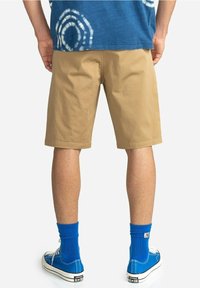 Khaki shorts met een ontspannen pasvorm, gemaakt van katoen, en met een lengte boven de knie. Gecombineerd met blauwe canvas sneakers en bijpassende sokken.