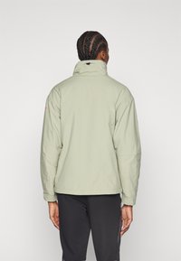 Veste légère vert clair, avec un col haut, des poignets élastiques et une subtile touche de rose sur l'épaule, vue de dos.