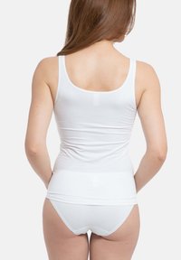 Top bianco senza maniche realizzato in tessuto liscio con sottili spalline, abbinato a biancheria intima bianca coordinata. La vestibilità è aderente al corpo, evidenziando la silhouette.