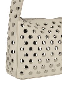 Bolso color crema hecho de cuero texturizado, adornado con tachuelas metálicas circulares distribuidas de manera uniforme por toda la superficie, con cierre de cremallera.