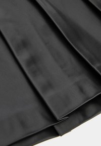 Juodas plisuotas dirbtinės odos audinys su lygiu paviršiumi ir matomu blizgesiu, rodantis kelis raukšles ir tvarkingą, struktūruotą kraštą.