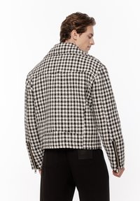 Czarny i biały kurtka w kratkę z wyraźnym kołnierzem, fakturowana tkanina, boczne zamki błyskawiczne i krótki krój. Widok z tyłu podkreśla kształt.