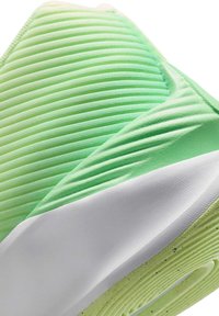 Gros plan d'un tapis de yoga roulé avec une surface texturée verte et une sangle blanche qui le maintient, sur fond blanc.