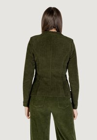 Tmavě zelený kordový blazer s vertikálním žebrováním, upnutý střih, dlouhé rukávy, doplněný o odpovídající kalhoty, viděný zezadu.