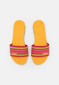 Gula gummisandaler med en texturerad sula, utrustade med ett flerfärgat randigt tygband i rosa, orange och grått. Dekorativ logotyp finns.