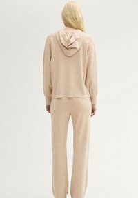 Sudadera de punto beige con una textura sutil, que cuenta con capucha, hombros caídos y pantalones de pierna ancha a juego, creando una silueta relajada.